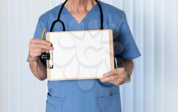 Senior male caucasian doctor with stethoscope in medical scrubs and holding clipboard for message