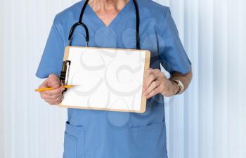 Senior male caucasian doctor with stethoscope in medical scrubs and holding clipboard for message with pencil for emphasis