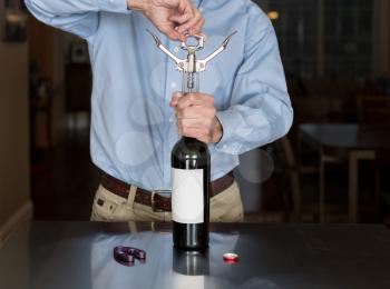 Senior caucasian man standing in kitchen opening bottle of red wine with a blank label for copy space