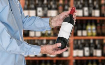 Senior caucasian wine steward offering a bottle of red wine with blank label to a customer in a wine store or winery. The bottle is ready with copy space.