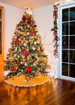 Ornately decorated christmas tree in the corner of a modern living room with cover under the branches