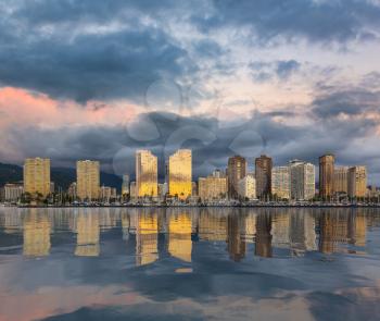Panorama of the skyline of Honolulu and Waikiki from Ala Moana park as the sun sets with artificial reflection in water surface