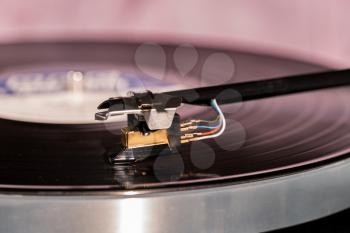 Side view of a playing vinyl record on vintage hi-fi stereo turntable with tonearm and cartridge in tracks of the LP