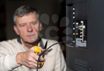 Close up of senior caucasian retired man cutting the aerial connection to his TV to illustrate cutting the cord