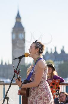 LONDON, UK - OCTOBER 1, 2015: Busker Emily Lee performing with guitar by side of River Thames in London, England