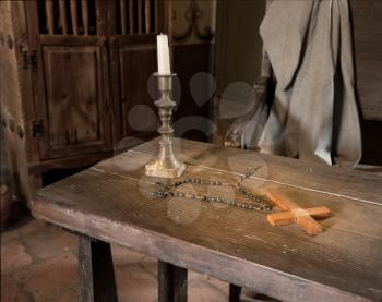 Ancient historic table with cross, rosary and candlestick to illustrate early priest life