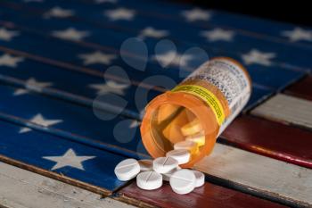 Oxycodone is the generic name for a range of opoid pain killing tablets. Prescription bottle for Oxycodone tablets and pills on wooden  USA flag