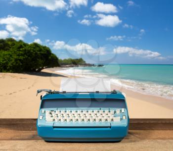 Modern electric typewriter on wooden desk with ocean beach background suggesting deserted island