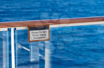 Warning sign Do Not Throw waste overboard on the teak railing of cruise ship above the ocean
