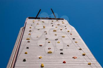 View up the front of a tall wooden artificial climbing wall to the safety ropes