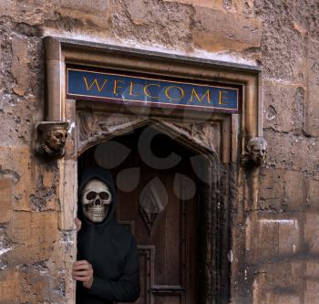 Halloween theme of man with skull in entrance doorway to old stone building welcoming visitors to haunted house
