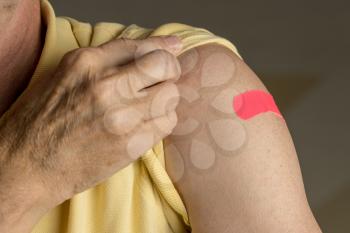 Senior caucasian man holding up shirt sleeve to show the bandaid after a flu jab in shoulder