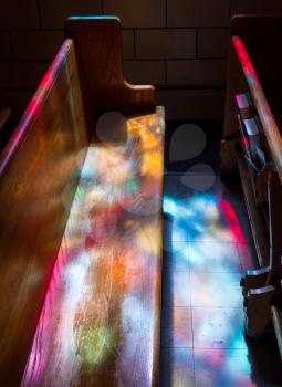Wooden bench pews illuminated by light from stained glass window