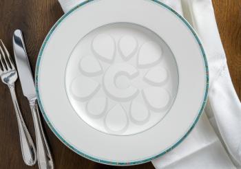 Round dinner plate with knive and fork on white napkin and wooden table flat lay