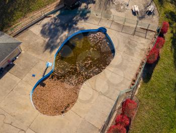Aerial drone point of view of an uncovered swimming pool filled with fallen leaves in the autumn after wind and storms