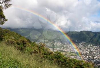 Bright rainbow over the suburbs of Woodlawn and Manoa in a valley above Honolulu on Hawaii