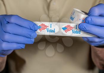 Hands in medical gloves holding roll of I Voted buttons with USA Flag ready for in person voters in Presidential election