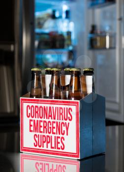 Six pack of brown beer bottles in box with Coronavirus Emergency Supplies stamped on side. Cold fridge out of focus in rear. Humorous view of hoarding