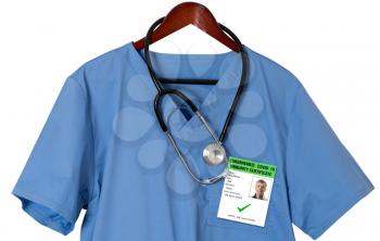 Blue medical scrubs uniform shirt on a hanger with stethoscope and badge for coronavirus immunity certificate
