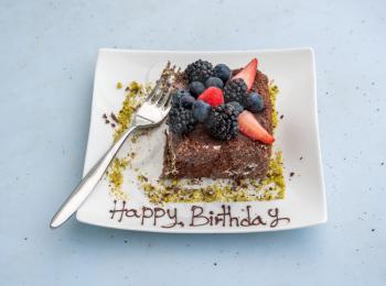 Happy Birthday on white place by remains of fresh fruit covered chocolate cake with fork
