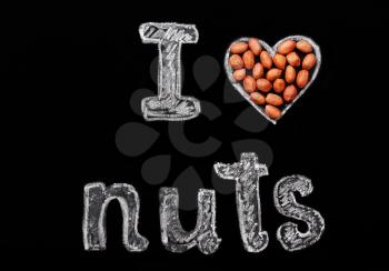 Peanuts on a black background and chalk inscription I love nuts. Heart drawn in chalk and peanuts.