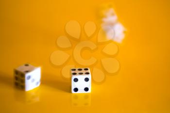 Three simple game cube cast on a bright yellow background. One cube has already stopped and two are still spinning