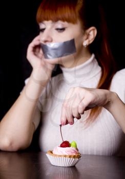 The girl, whose mouth sealed with tape sad looking at cake