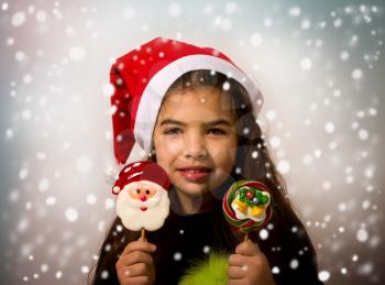 A little girl in a Santa Claus hat holds bright New Year candies in snowflakes