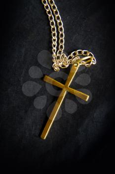 a simple metal cross on a chain lies against a black background