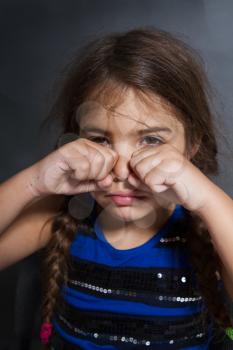 a little girl with two pigtails sits and weeps bitterly on a grubby gray background