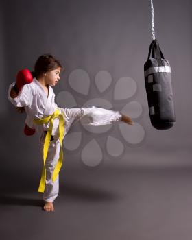 little girl in a kimono and with a yellow belt trains and beats a ponchig bag