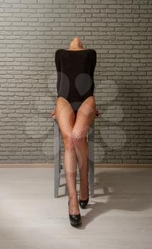young sexy girl with wet red hair in a black sports bodysuit and mesh pantyhose on a rough wooden stool against a gray brick wall