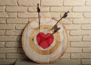 Handmade rough wooden target with a center in the form of a red heart and an arrow from a bow that hit the center and two arrows missed.
