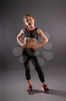 little girl in sportswear doing gymnastics and posing against a dark background