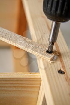Electric screwdriver twists screw in a wooden structure close-up