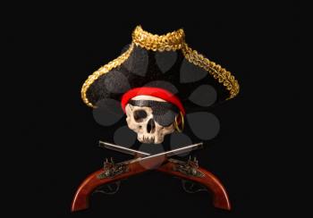 Skull in a traditional wide-brimmed pirate cocked hat with two pistols on a dark background