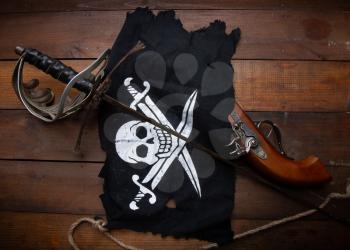 pirate flag jolly roger sword and pistol lying on a dark wooden surface