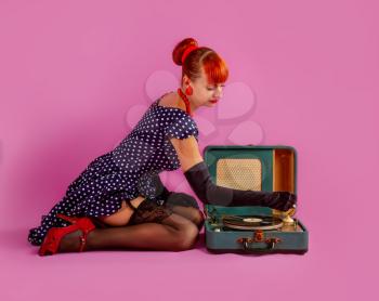 young girl in a stylish retro dress and stockings is listening to a record on an old gramophone