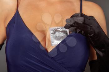 Young girl in a dark blue dress and high silk gloves pulls a condom from the neckline