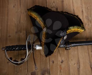 Classic pirate black felt captain's cocked hat and scabbard sword lying on a wooden background