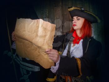 Young attractive armed girl pirate captain considers map against flag background Jolly Roger