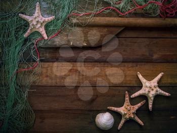 old wooden boards on top of which lies a fishing net with starfish and an oar. With place for your text.
