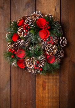 beautiful Christmas wreath of cones of paper flowers and fir branches hanging on a rough wooden surface