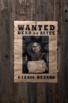 old wanted poster nailed to a rough wooden wall with a portrait of the criminal and a promise of reward