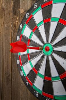 darts target hanging on an old wooden wall with a red arrow hitting her exactly in the center