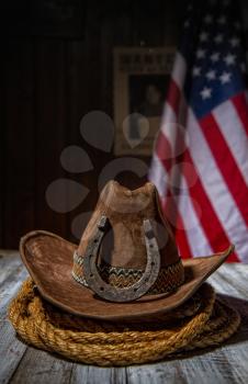 Classic cowboy hat and lasso lie on a wooden table against the background of the US flag and the poster for the search for the criminal in the sheriff s office.