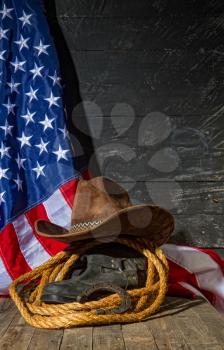 classic cowboy wide-brimmed brown brown lasso hat made of coarse rope and riding boots on a dark wooden background next to the US flag