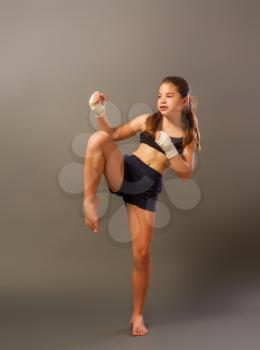 little girl in a sports tank top and shorts with hands wrapped in protective bandage is engaged in martial arts on a dark background