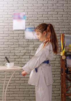 A little girl in a white kimono with a blue belt takes karate lessons via the Internet while at home on self-isolation during quarantine