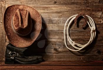 Very rusty old horseshoe symbol of good luck and lasso hanging on a wooden wall cowboy hat and boots